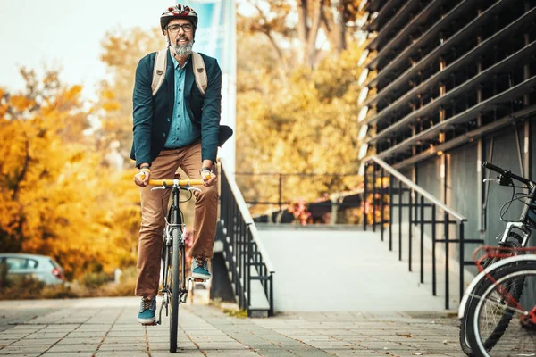 自転車で事務所に行くのはハンサムなカジュアルな中年のビジネスマンです オフィス街の前で自転車を運転している — ストック写真
