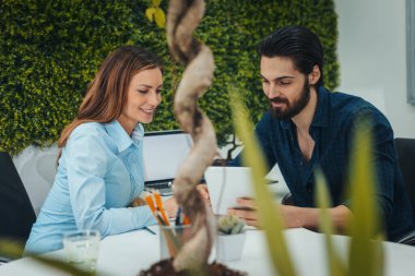 Genç başarılı tasarımcılar ofiste dijital tablet kullanıyorlar. Projeyi analiz ediyorlar ve konuşuyorlar..