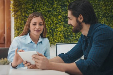 Genç başarılı tasarımcılar ofiste dijital tablet kullanıyorlar. Projeyi analiz ediyorlar ve konuşuyorlar..