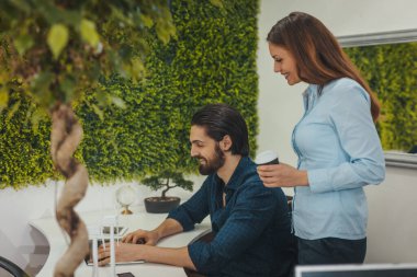 Genç başarılı tasarımcılar bir dizüstü bilgisayar üzerinde çalışıyorlar ve ofiste proje hakkında konuşuyorlar..