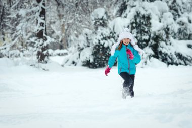 Kışlık giysiler içinde şirin küçük mutlu kız, karlı kış gününde koşmaktan zevk alıyor..