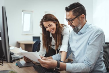 Başarılı gülümseyen genç meslektaşlar zirveye çıkan projeden bahsediyorlar. Ofiste bir belgeye bakıyorlar..