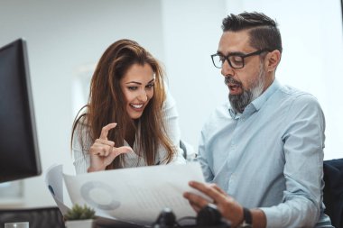 Başarılı gülümseyen genç meslektaşlar zirveye çıkan projeden bahsediyorlar. Ofiste bir belgeye bakıyorlar..