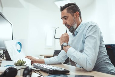 Ciddi düşünceli bir adam zirveye çıkan bir projeye bakıyor. Ofiste bir belgeye bakıyor..