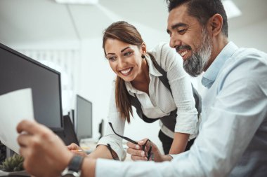 Başarılı gülümseyen genç meslektaşlar zirveye çıkan projeden bahsediyorlar. Ofiste bir belgeye bakıyorlar..