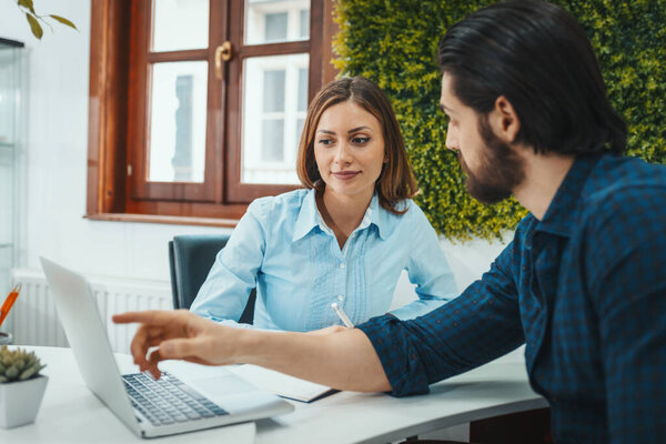 Young successful designers are talking about project at the office. A man is talking about project exposed on a laptop, and young woman listens her colleague.