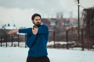 Aktif bir genç adam, eski fabrikada, dışarıda kış eğitimi sırasında eski demiryolları arasında esniyor ve tatbikat yapıyor..  