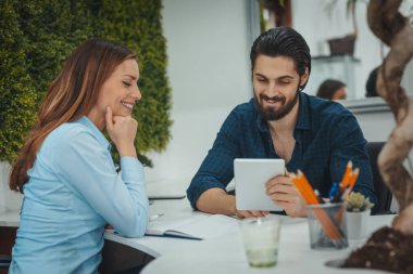 Genç başarılı tasarımcılar ofiste dijital tablet kullanıyorlar. Projeyi analiz ediyorlar ve konuşuyorlar..
