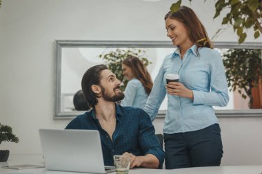 Genç başarılı tasarımcılar bir dizüstü bilgisayar üzerinde çalışıyorlar ve ofiste proje hakkında konuşuyorlar..