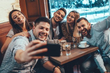 Bir grup arkadaş bir kafede akıllı telefonla selfie çekiyor..