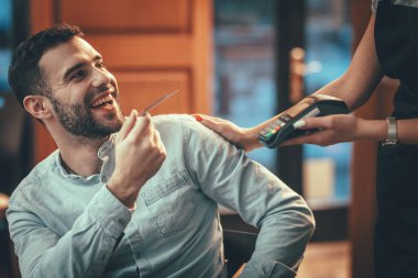 Yakışıklı bir genç, bir kafede kahveye kredi kartıyla para ödüyor..