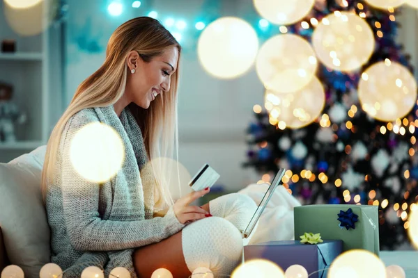 Mutlu genç kadın evde dinleniyor ve internetten Noel hediyeleri alıyor..