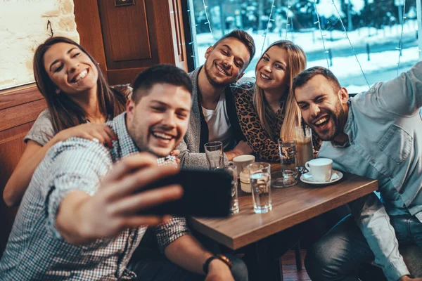 A group of friends is taking selfie with a smartphone in a cafe.