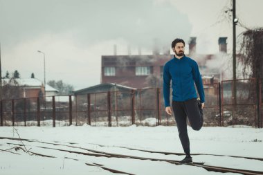 Aktif bir genç adam, eski fabrikada, dışarıda kış eğitimi sırasında eski demiryolları arasında esniyor ve tatbikat yapıyor..  