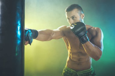 Concentrated handsome muscular man training hard hitting a boxing bag. clipart