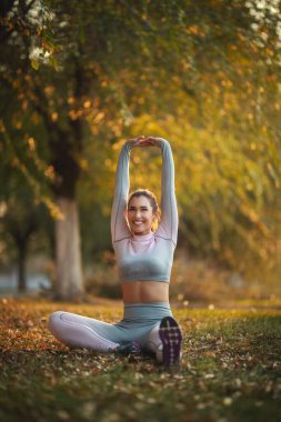 Spor giyimli mutlu kadın güneşli bir günde doğada esneme egzersizleri yapıyor..