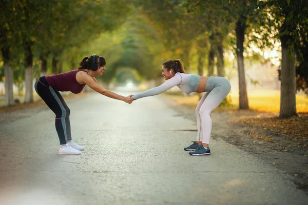快乐的两个姐姐正在做热身运动 然后沿着阳光灿烂的大道跑去 — 图库照片