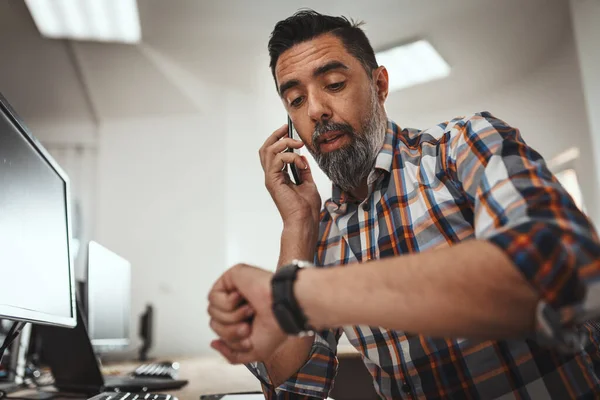 オフィスで働いている間 ハンサムな成功した起業家は携帯電話で話しています 彼は遅れないように時計を見ている — ストック写真