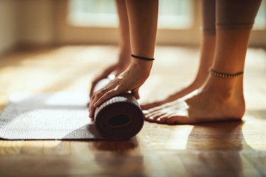 Bir kadının ellerine yaklaşmak egzersiz minderini sarmak ve yoga yapmaya hazırlanmaktır. Evde sabah güneşinde paspasın üzerinde egzersiz yapıyor..