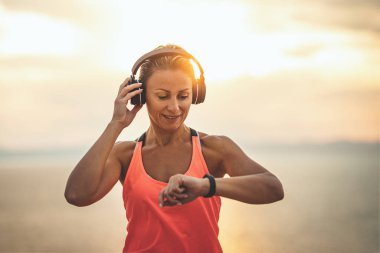 Güzel bir genç kadın gün doğumunda deniz kenarında esneme egzersizi yapmaya hazır kulaklıkla müzik dinliyor..