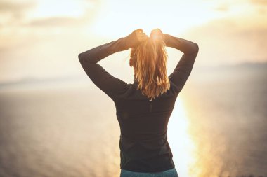 Güzel bir genç kadın gün doğumunda deniz kenarında esneme egzersizi yapıyor..