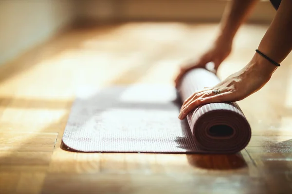 Close up of a womans hands is rolling up exercise mat and preparing to doing yoga. She is exercising on floor mat in morning sunshine at home.