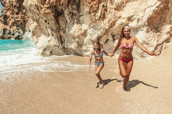 美しい少女は母親と一緒にビーチで楽しんでいます 彼らは海岸を走り 楽しんでいます — ストック写真
