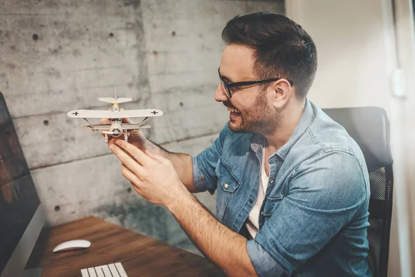 年轻而成功的快乐的自由职业企业家正在享受乐趣 展示很少的飞机模型 解释它是如何飞行的 — 图库照片