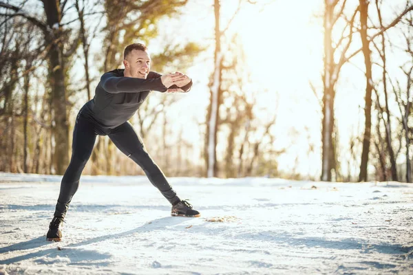 Aktywny Młodzieniec Wykonuje Ćwiczenia Rozciągające Leśnej Drodze Podczas Zimowego Treningu — Zdjęcie stockowe
