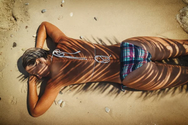 晴れた日には美しい若い女性がビーチでリラックスしています ヤシの木の陰で 砂の上に倒れている — ストック写真