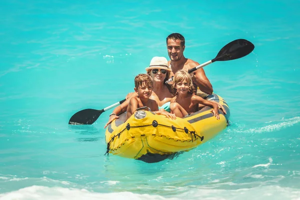 幸せな家族はゴム製のカヤックに乗って楽しんでいます そして波は夏休み中に熱帯の海の水でそれらを飛び散っています — ストック写真