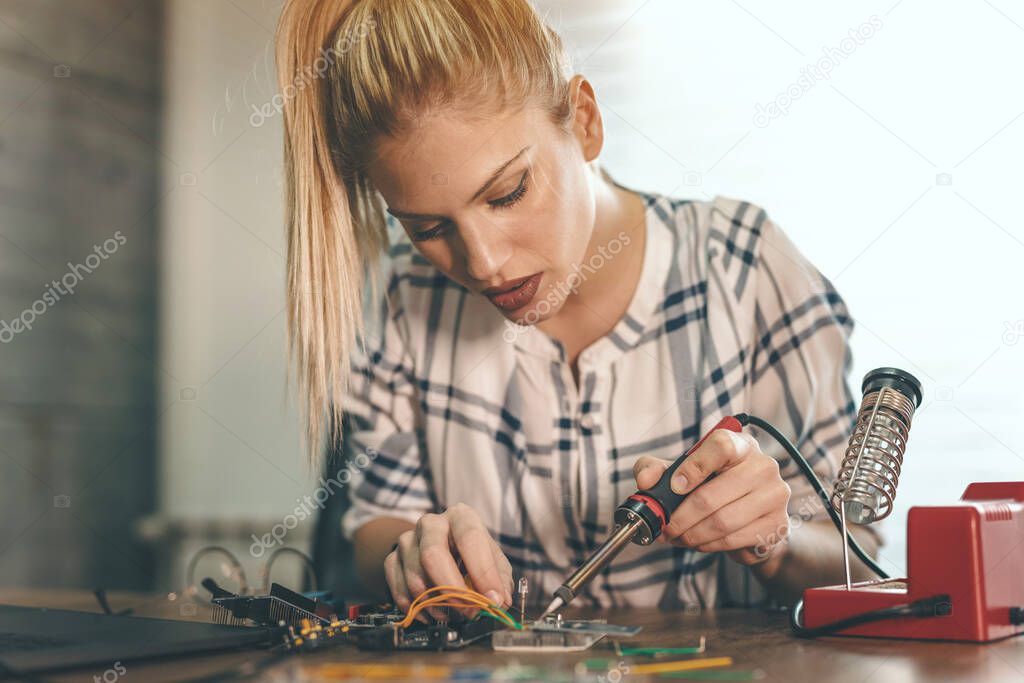 Young woman technician is focused on the repair of electronic equipment by soldering iron.