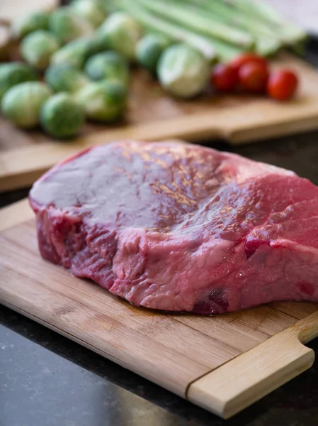 Vista de perto de pedaço fresco de carne com alguns vegetais na parte de trás — Fotografia de Stock