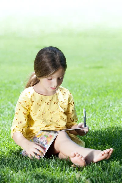 Portrait of little girl studying on the grass in summer environment — Stock Photo, Image