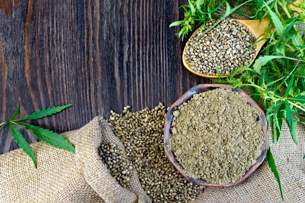 Flour hemp in bowl and seed in wooden spoon on board — ストック写真