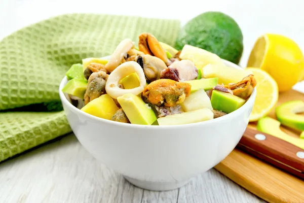 Salad with seafood and lemon in bowl on light board — Stockfoto