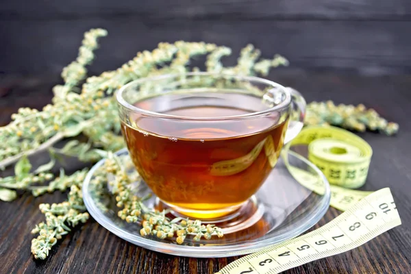 Té con ajenjo en taza de vidrio y metro en tablero oscuro —  Fotos de Stock