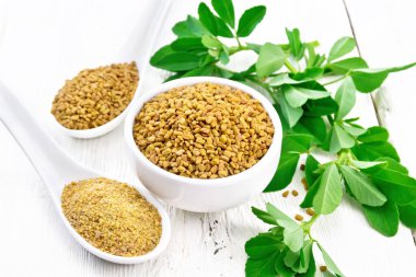 Kavanozda FenuGreek ve ışık panosunda yaprakları olan iki kaşık.