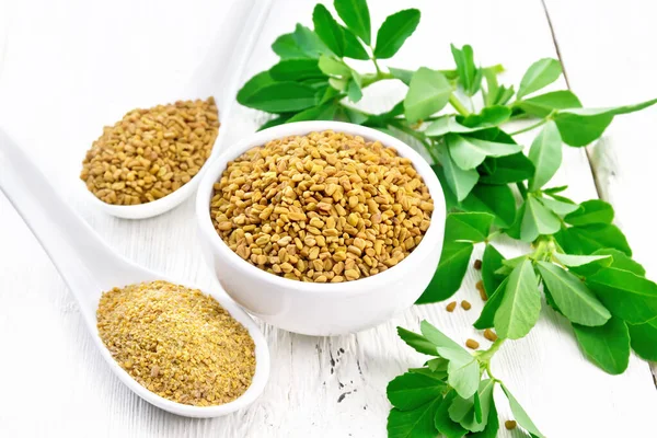 Fenugreek in bowl and two spoons with leaves on light board — ストック写真