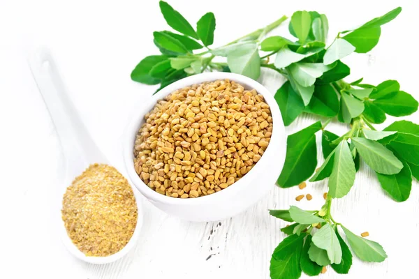 Fenugreek in bowl and spoon with leaves on board — Stock Photo, Image
