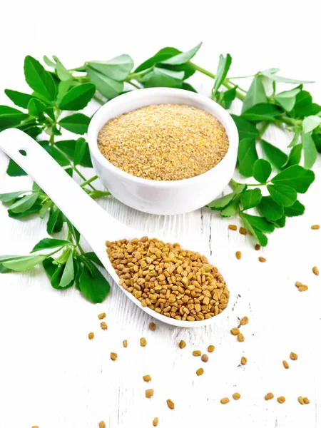 Fenugreek in spoon and bowl with leaves on white wooden board — ストック写真