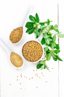 Kavanozda FenuGreek ve üzerinde yapraklar olan iki kaşık.