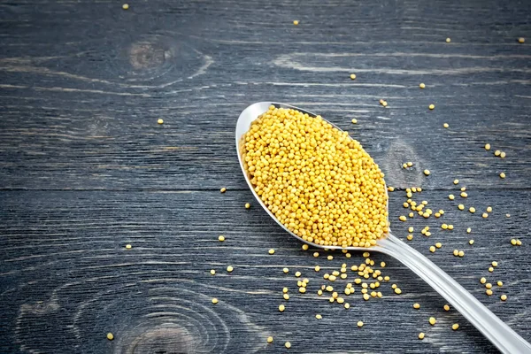 Mustard seeds in metal spoon on board — Stock Photo, Image