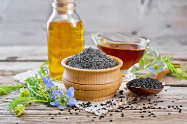 Kâsede siyah et unu, kaşıkta tohum, şişede yağ ve çuval bezinde sos, mavi çiçekli Nigella sosu ve tahtanın üzerinde yapraklar.