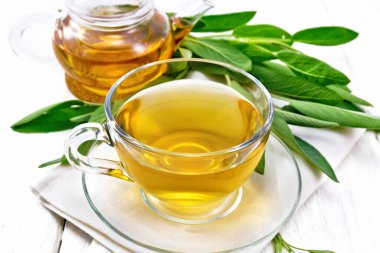 Cam bardakta adaçayı ve tahta zeminde havlunun üstünde çaydanlık.