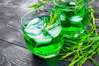 İki bardakta buzlu tarhun limonatası, tahta bir arka planda östrogon dalları.