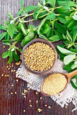 Ground fenugreek in a spoon and seeds in a bowl on burlap with green leaves on wooden board background from above clipart