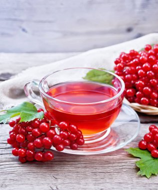 Cam fincanda viburnum, böğürtlenli hasır tabakta yeşil yapraklar ve tahta arka planda çuval bezi olan çay.