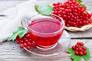 Cam bardakta viburnum, böğürtlenli hasır tabakta yeşil yapraklar ve tahta arka planda çuval bezi olan çay.