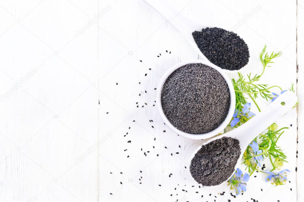 Flour and seeds of black caraway in bowls, sprigs of kalingini with blue flowers and green leaves on a white wooden board background from above